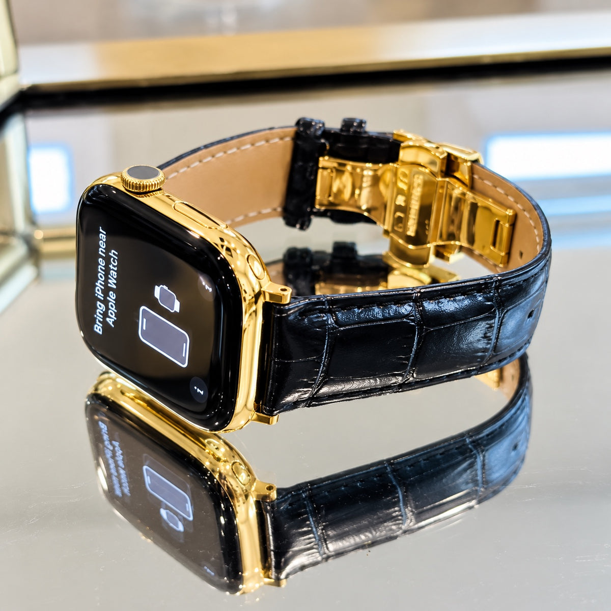Custom Apple Watch Series 12 in 18K gold with black alligator leather band and deployant buckle on a mirrored display