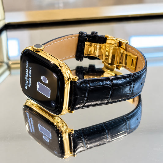 Custom Apple Watch Series 12 in 18K gold with black alligator leather band and deployant buckle on a mirrored display